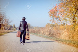 33648714-Young-man-musician-in-retro-hat-and-leather-jacket-with-vintage-suitcase-and-guitar-walking-away-on--Stock-Photo